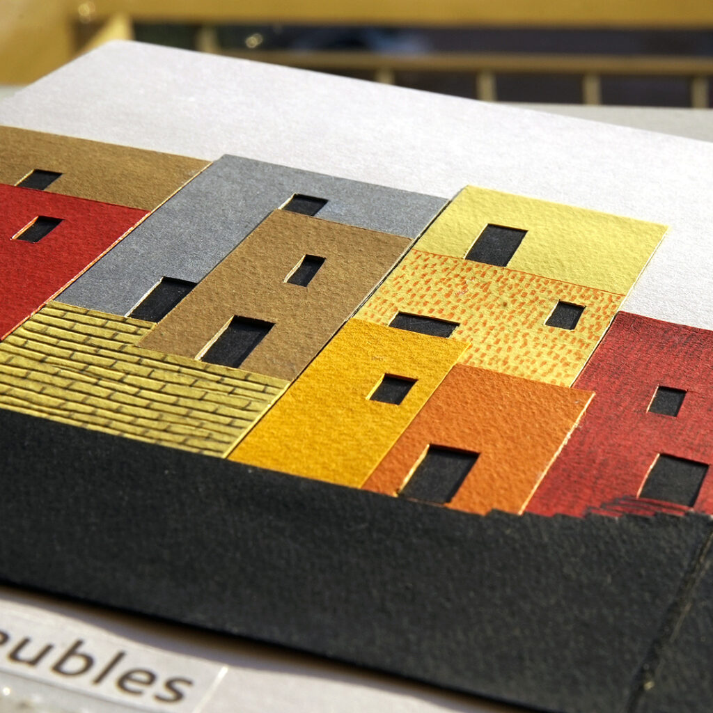 Photograph of a collage of papers of different colours representing buildings, with doors and windows cut-out.