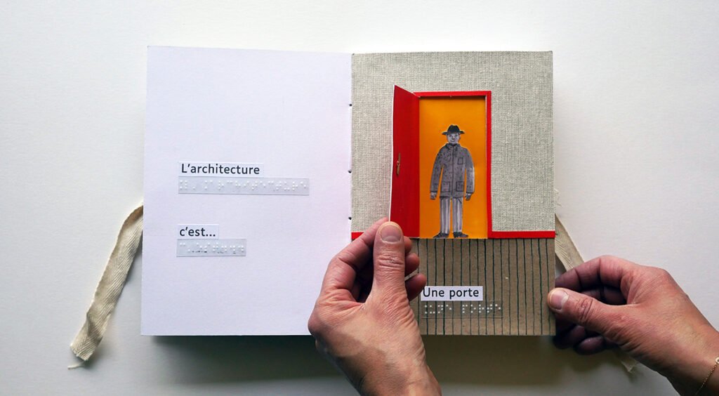 Photographie d'un livre tactile ouvert. Des mains ouvre une porte rouge. Un personnage est debout derrière la porte.